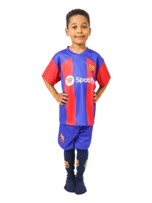 Chłopiec w kompletnym stroju piłkarskim Barcelona, który obejmuje koszulkę spodenki i getry